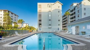 A swimming pool with lounge chairs, a speed limit sign, and a building with balconies. - Bac Bay #223 (Fort Myers Beach)