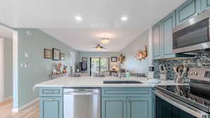 A modern kitchen with teal cabinetry, stainless steel appliances, a dishwasher, and a large island with a sink. - Bac Bay #223 (Fort Myers Beach)