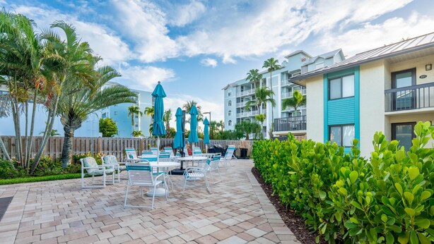 A patio area with outdoor seating, palm trees, and a building with balconies. - Bac Bay #223 (Fort Myers Beach)