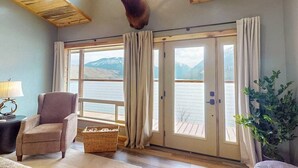 Una habitación con un ventanal grande, una silla, una lámpara y la cabeza de un animal montada.