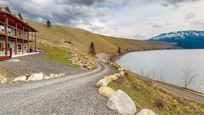 Un camino de grava que conduce a una edificación de madera con vistas a un lago y montañas.