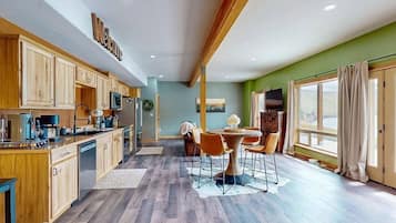 A spacious kitchen with wooden cabinets, a dining area with a round table and chairs, and a large window with curtains.