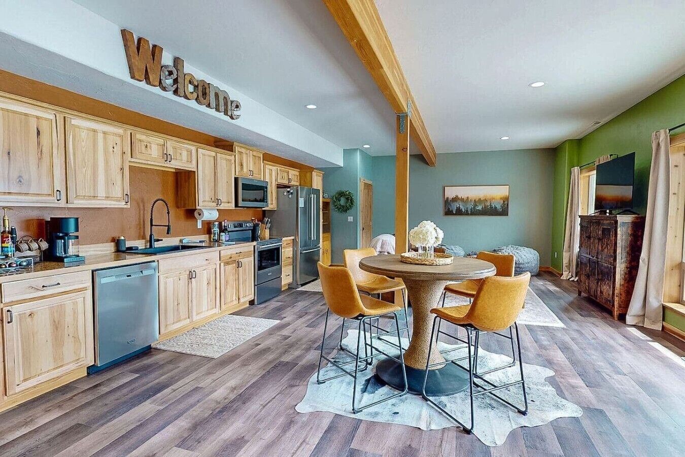 A modern kitchen with wooden cabinets, a central island, and a 'Welcome' sign.