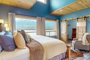 A bedroom with a large bed, a chair, a wooden door, and a view of mountains. - 20 Moraine Tranquility Lodge  (upstairs unit) (Joseph)