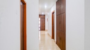 A corridor with wooden doors, white walls, and tiled flooring. - Single Roomsixmile Guwahati (Guwahati)