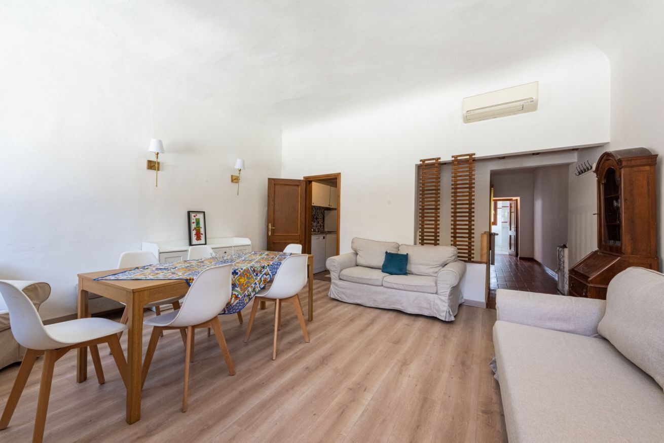 A spacious living area with a dining table, chairs, a sofa, and a wooden ladder.