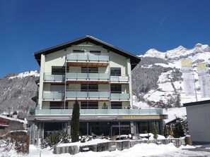 A multi-story hotel with balconies, a sign indicating 3.5 rooms, and a view of snow-covered mountains. - Bärenbächli Appartement/Fewo 6-Bettwohnung by Interhome (Engelberg)