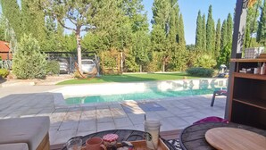 Un área de comedor al aire libre con vista a la piscina, mobiliario de madera y una mesa lista para el desayuno.