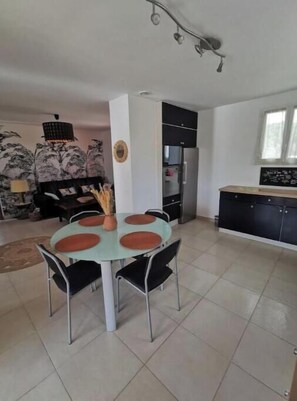 A dining area with a round table, chairs, and a kitchen in the background. - 2-bedroom apartment with terrace, pool and jacuzzi near the center (Le Cannet-des-Maures)