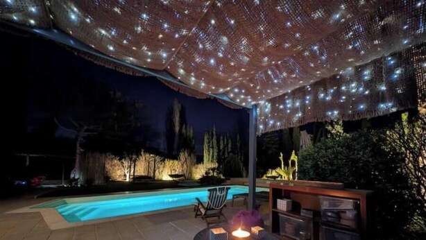 Un patio exterior con piscina, una mesa con velas y luces colgantes.