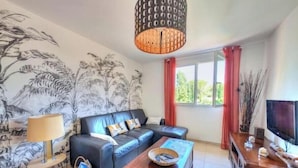 Una sala de estar con un sofá, una mesa de centro, una lámpara, un televisor y una pared con un mural floral.