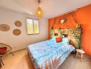 A bedroom with a bed, a chair, a stool, a hanging light fixture, and a wall with a circular pattern. - 2-bedroom apartment with terrace, pool and jacuzzi near the center (Le Cannet-des-Maures)
