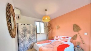 Un dormitorio con cama, lámpara colgante, un adorno en la pared y una ventana con cortinas.