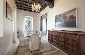 Un coin repas avec une table en verre, des chaises blanches, un lustre et un grand tableau accroché au mur.