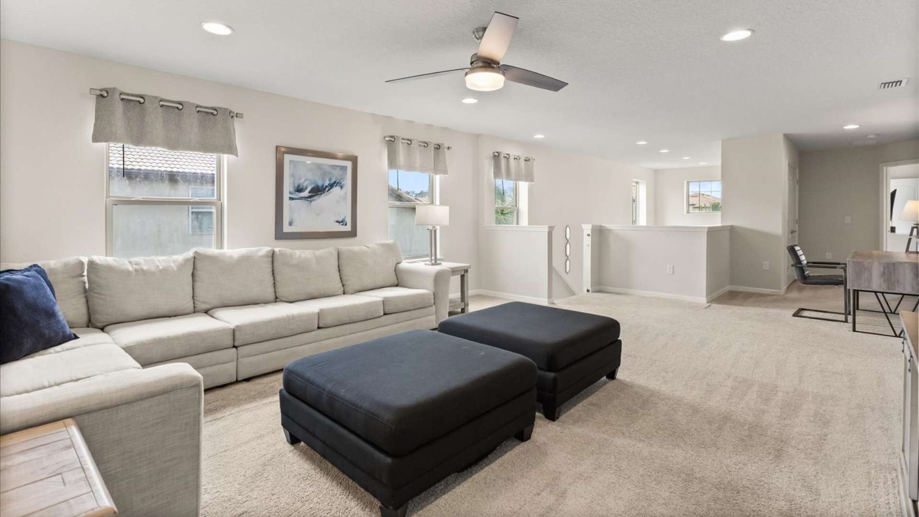 A spacious living room with a sofa, ottomans, a dining table, and a ceiling fan.
