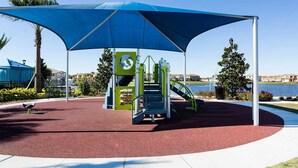 Ein Spielplatz mit einem blauen Baldachin, rotem Gummiboden und einer grünen Kletterkonstruktion.