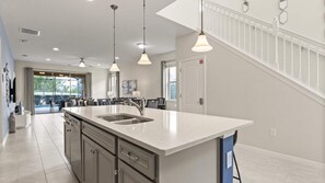 A modern kitchen with a large island, pendant lighting, and a view to a patio area. - Upstay- Family Villa for 12 w Pool Games BBQ (Kissimmee)