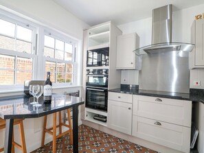 A modern kitchen with white cabinetry, a stainless steel range hood, and a window with a view of a brick building. - 19 Queen Street (Emsworth)
