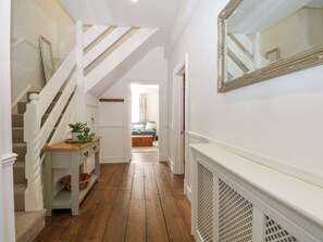 A hallway with wooden flooring, a staircase with white balusters, a console table with a plant, and a large mirror on the wall. - 19 Queen Street (Emsworth)