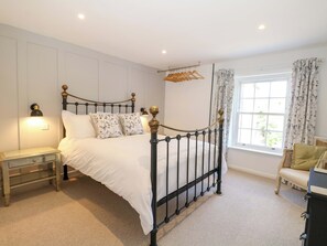 A bedroom with a four-poster bed, a nightstand, a dresser, a window with curtains, and a hanging rack. - 19 Queen Street (Emsworth)