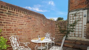 Eine Terrasse mit weißen Metallstühlen und einem Tisch, eine Ziegelwand und eine weiße Tür mit Fenster.