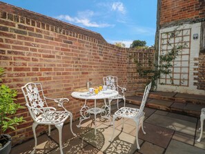 A patio with white metal chairs and a table, a brick wall, and a white door with a window. - 19 Queen Street (Emsworth)