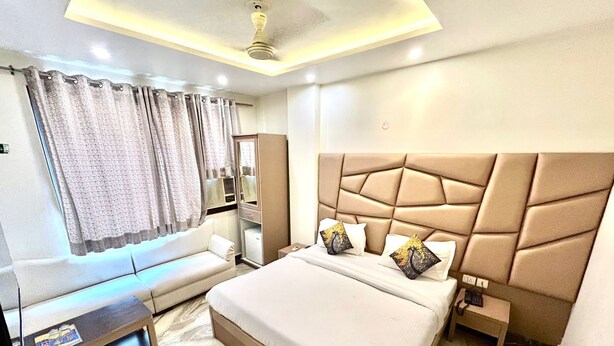 A modern hotel room with a large bed, a sofa, a small table, and a ceiling fan. - Hotel Amrit Villa Karol Bagh New Delhi (New Delhi)