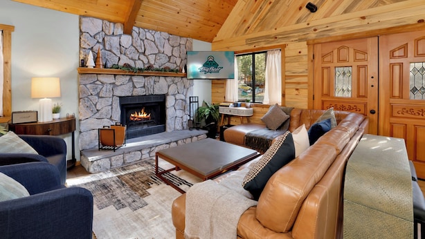 A cozy cabin interior with a stone fireplace, leather sofa, and wooden ceiling. - Hot Tub Cabin w/ Game Loft, Fireplace + Deck – Near Lake & Slopes (Big Bear Lake)