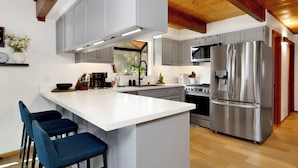 A modern kitchen with a central island, bar stools, stainless steel appliances, and a wooden ceiling. - Hot Tub Cabin w/ Game Loft, Fireplace + Deck – Near Lake & Slopes (Big Bear Lake)