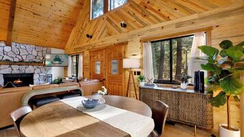 A wooden cabin interior with a stone fireplace, a dining area, and a kitchen.