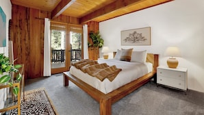 A bedroom with a wooden bed, a nightstand, a bedside table, a window with a view, and a plant. - Hot Tub Cabin w/ Game Loft, Fireplace + Deck – Near Lake & Slopes (Big Bear Lake)