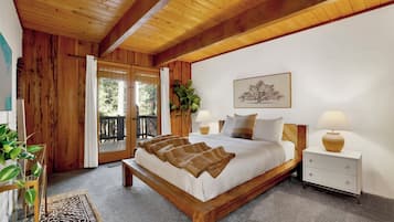 A bedroom with a wooden bed, a nightstand, a bedside table, a window with a view, and a plant.