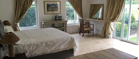A bedroom with a bed, a wooden table, a chair, a desk, and a window with curtains.