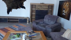 A living room with a mounted animal hide, a sofa, a coffee table with books, and a painting of a lion. - Cozy vacation apartment "Haus Bertram" in Leun. in a quiet rural location. (Leun)