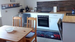 A modern kitchen with a wooden ceiling, white cabinets, a built-in oven, and a dining area with a table and chairs. - Cozy vacation apartment "Haus Bertram" in Leun. in a quiet rural location. (Leun)