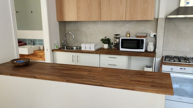 Una cocina moderna con armarios de madera, encimera blanca, microondas integrado y cocina a gas.