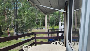 Un patio techado al aire libre con una mesa redonda y cuatro sillas, una valla de madera y vistas a un área boscosa.