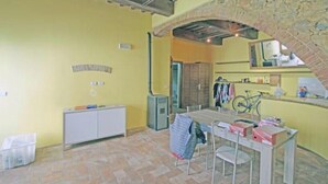 Una habitación con un arco de piedra, un armario blanco, una mesa con sillas y una bicicleta.