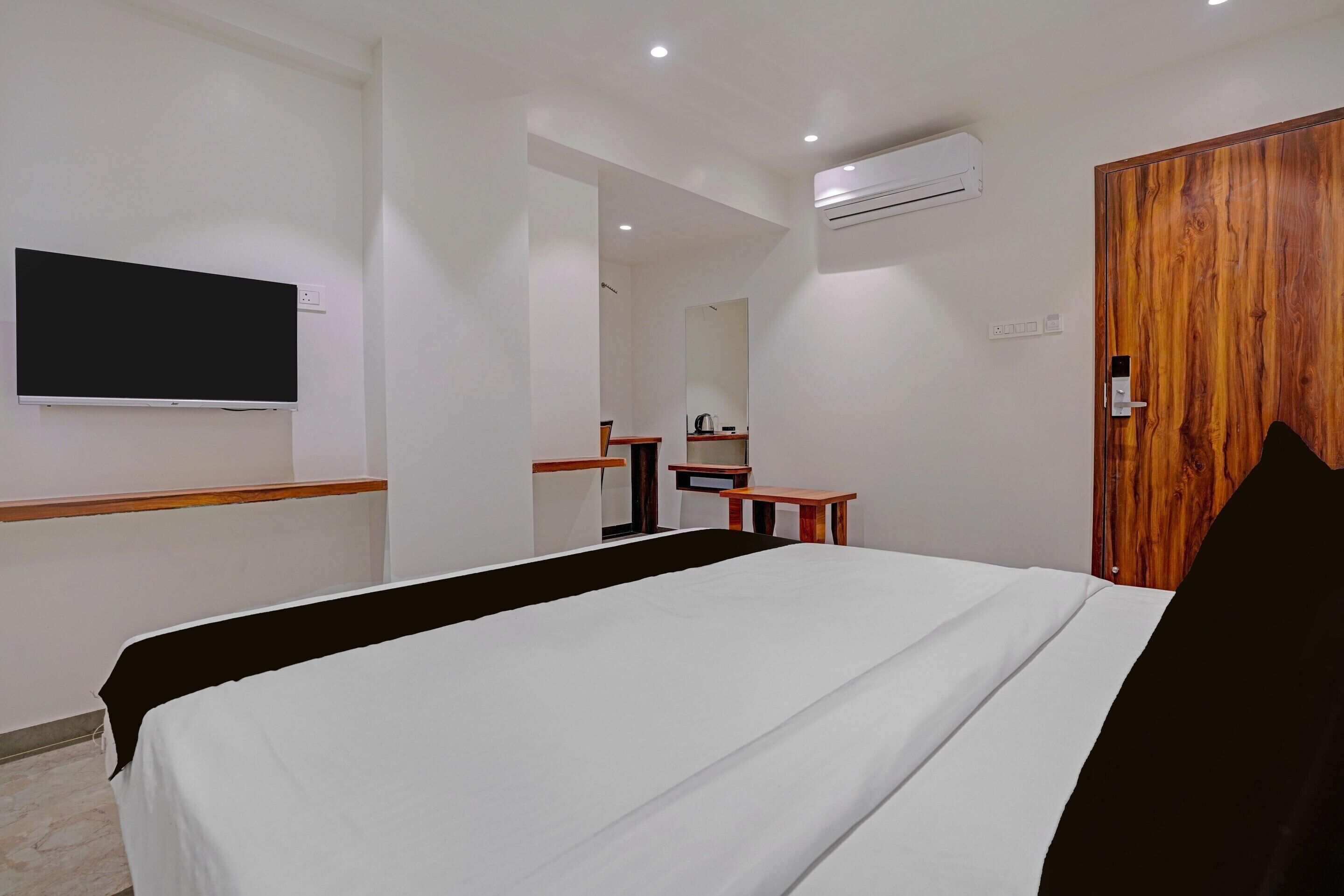 A hotel room with a bed, a television, an air conditioning unit, a wooden door, and a small table.