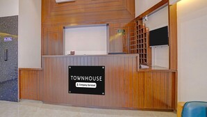 A reception desk with a sign reading 'TOWNHOUSE Company Serviced,' air conditioning units, a digital screen, and a small shelf with items. - Townhouse Skyboat XLO Point (Nashik)
