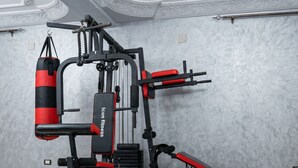 Un gimnasio con equipo de levantamiento de pesas, incluyendo mancuernas, un banco y un saco de boxeo.