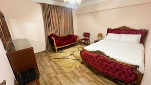 Habitación de hotel con suelo de madera, sofá tapizado en rojo, mesita de noche de madera, escritorio y cama con cabecero rojo.