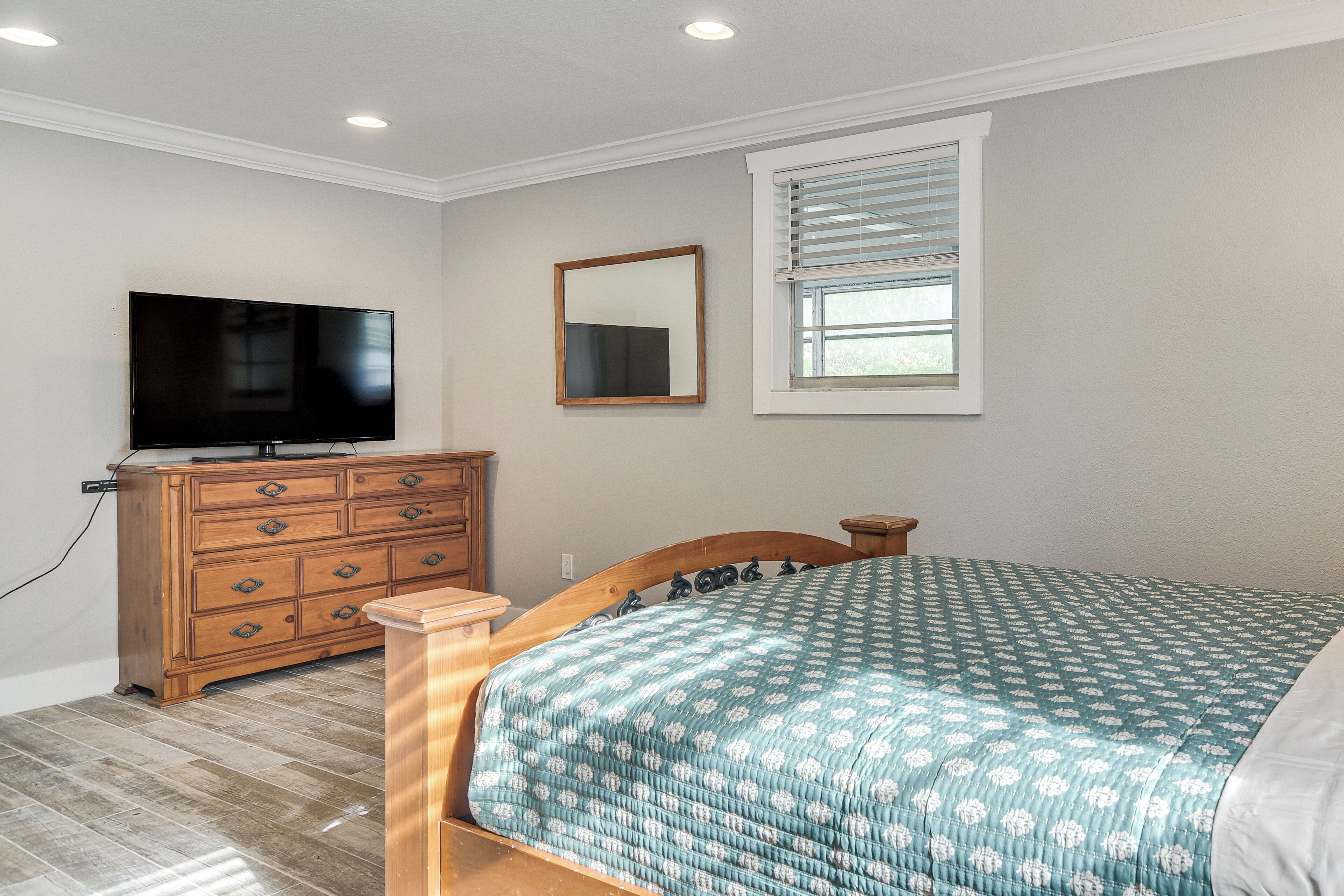 A bedroom with a bed, dresser, television, and a window with blinds.