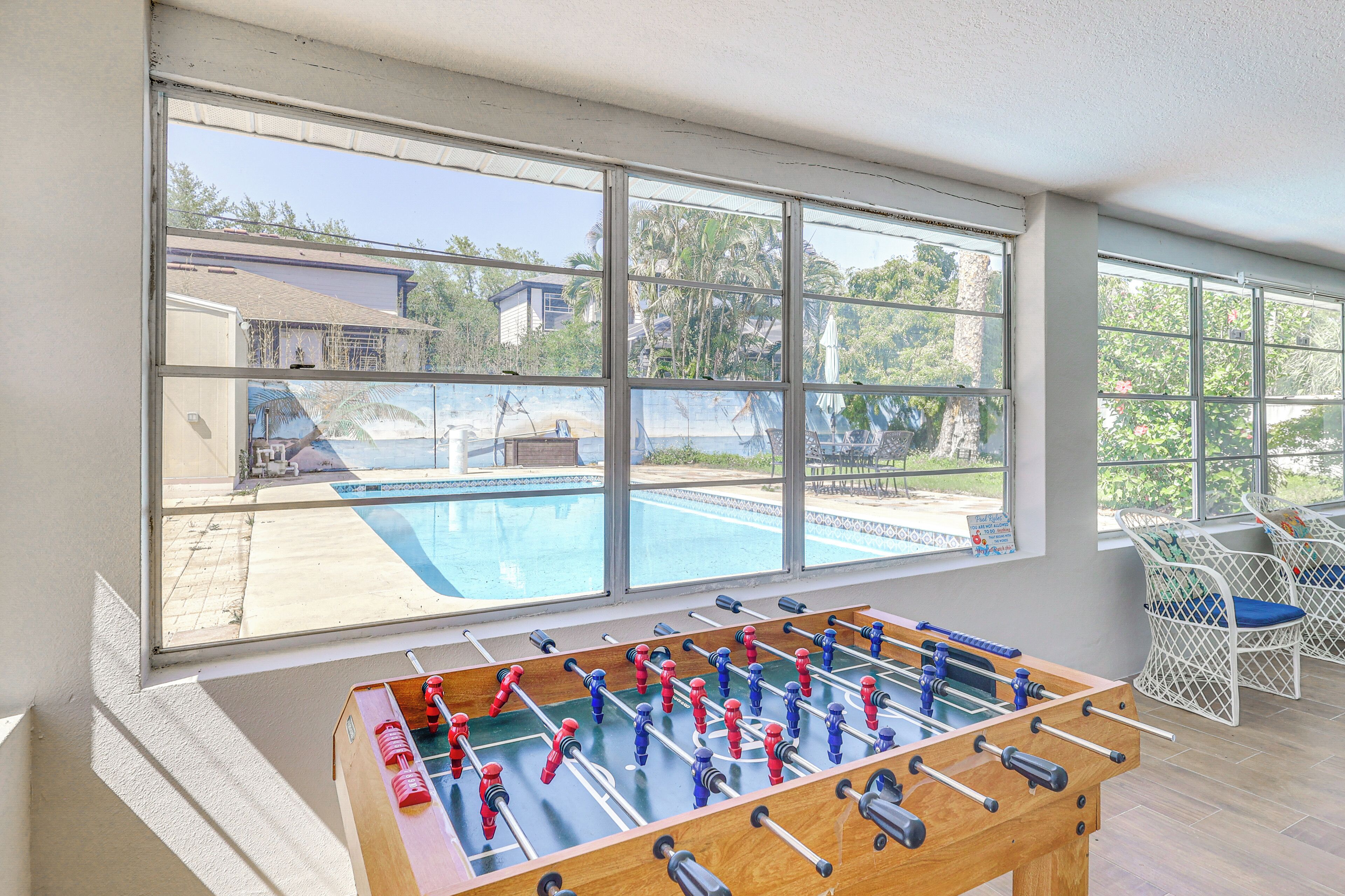 Una habitación con mesa de futbolín, ventanas amplias y vista a una piscina.