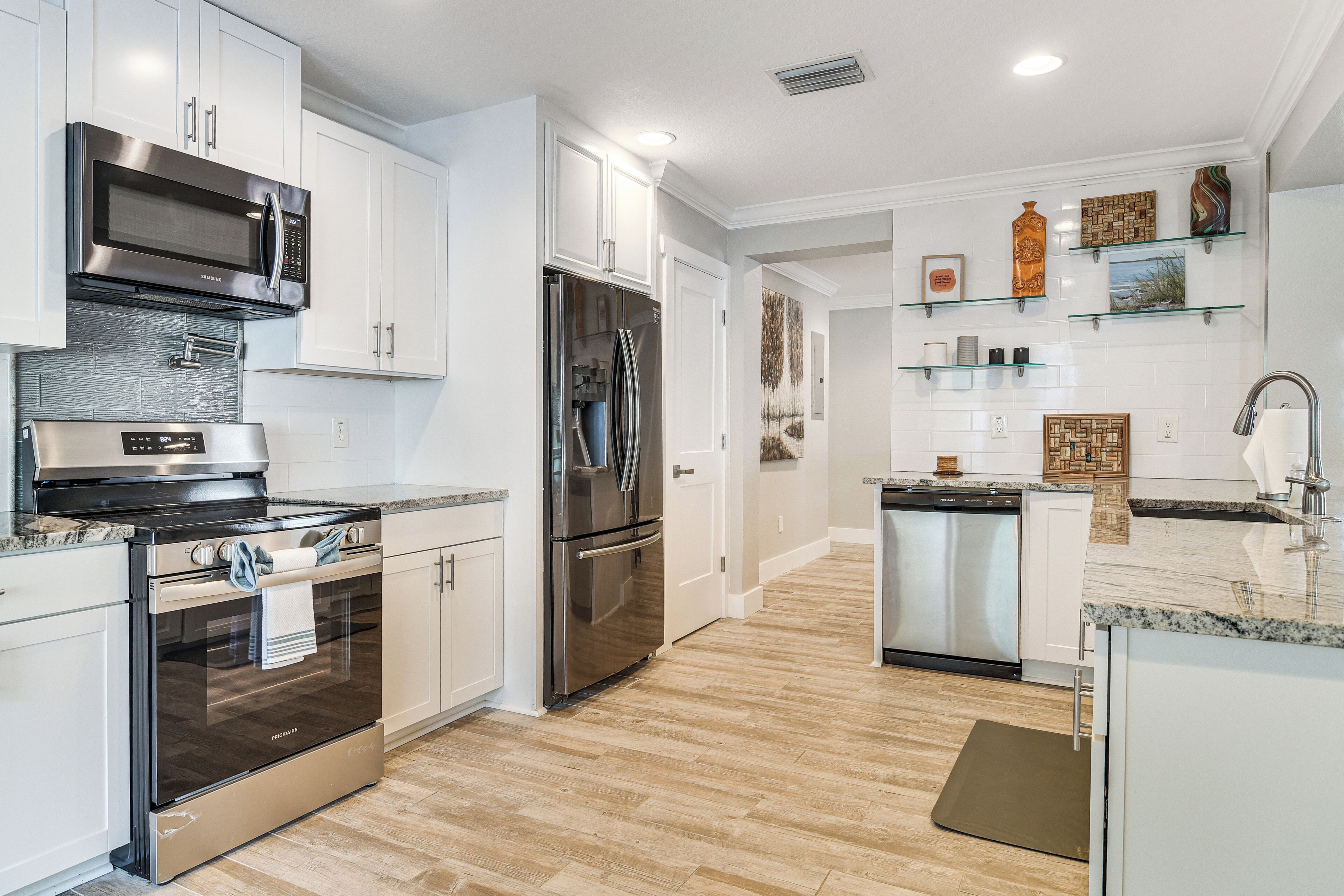 A modern kitchen with stainless steel appliances, white cabinetry, and a hardwood floor.