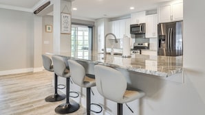 A modern kitchen with a granite countertop, stainless steel appliances, and a bar area with bar stools. - Steps to Bayshore Blvd! Snowbird Retreat w/ Pool (Tampa)