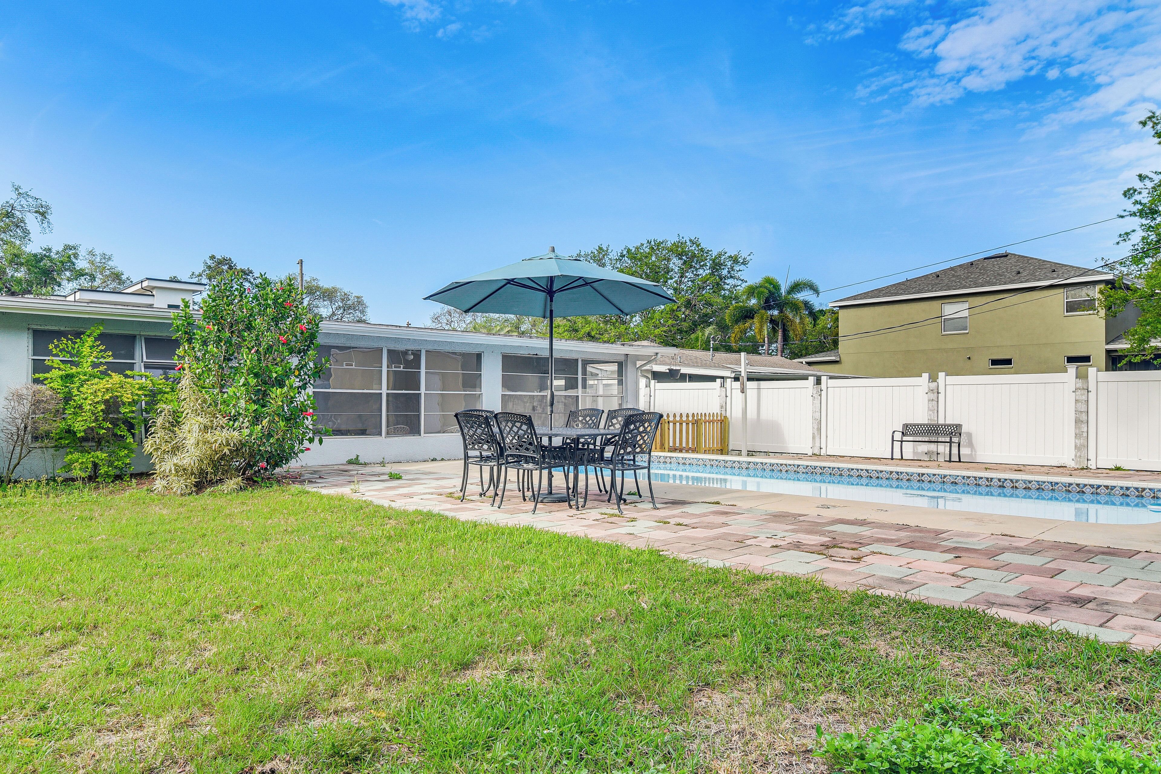 A backyard with a swimming pool, a patio table with chairs, and a covered seating area.