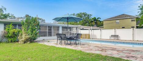 A backyard with a swimming pool, a patio table with chairs, and a covered seating area.