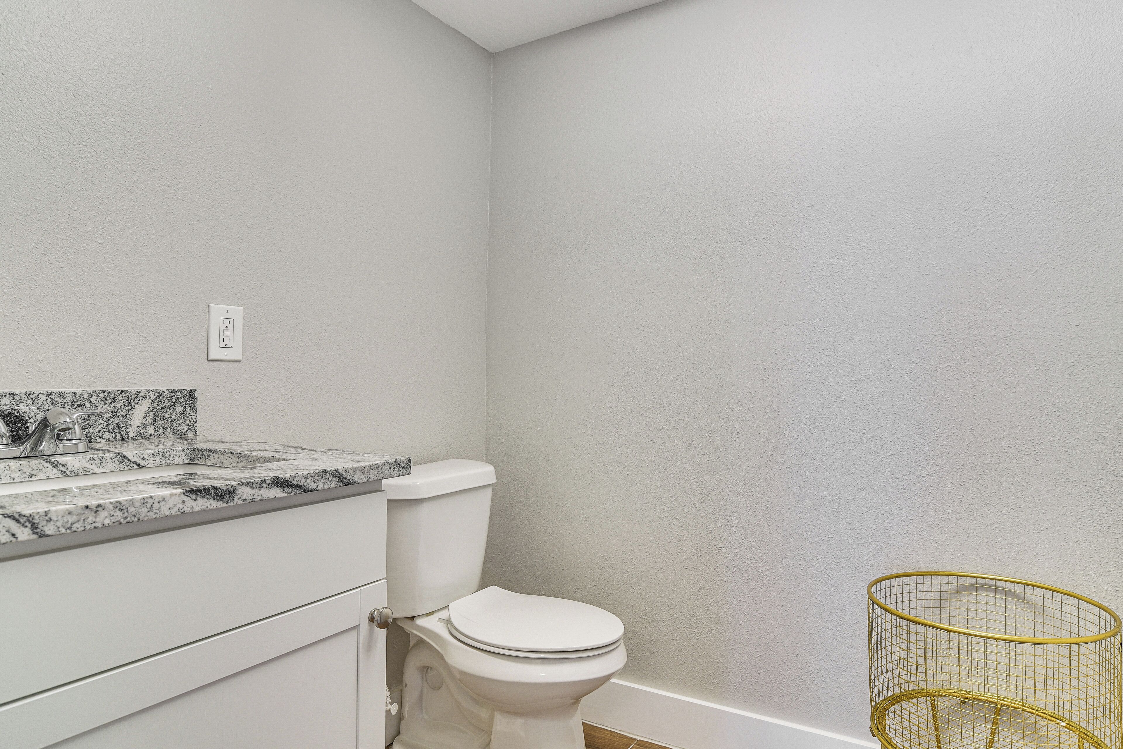 A bathroom with a toilet, sink, and a gold wire basket.