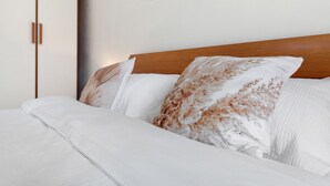 Een net opgemaakt bed met witte lakens en een bruin kussen met bloemenprint, een houten hoofdbord en een wanddecoratie.